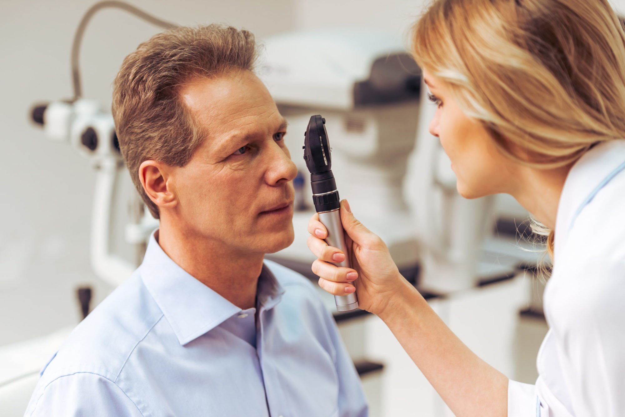 At The Ophthalmologist Young beautiful female ophthalmologist examining handsome middle aged man with modern equipment,close-up